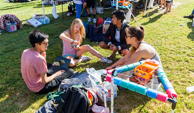 Students sitting on a lawn working on a project .