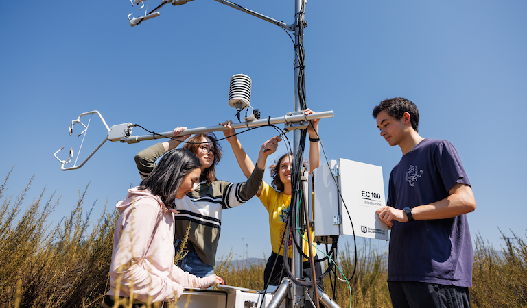 Four students working on atmospheric monitoring equipment outside