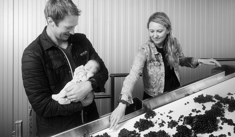 Christopher Strieter holding baby next to grape sorting conveyor