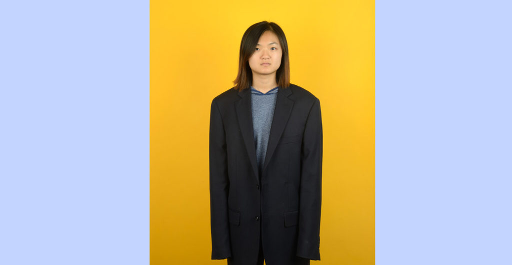 Image of girl in man's suit looking at camera to advertise 2018 Fall Semester Exhibition at Harvey Mudd College