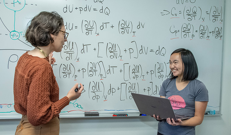Faculty member and student with computer talk in front of whiteboard with math problems