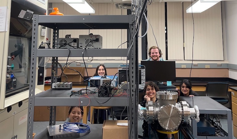 Prof. Hernandez-Castillo and students posing within lab shelving