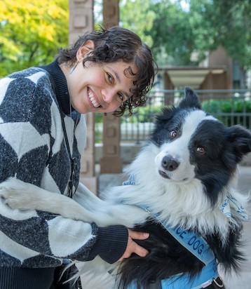 Professor in black and white sweater holding her black and white service dog's paw