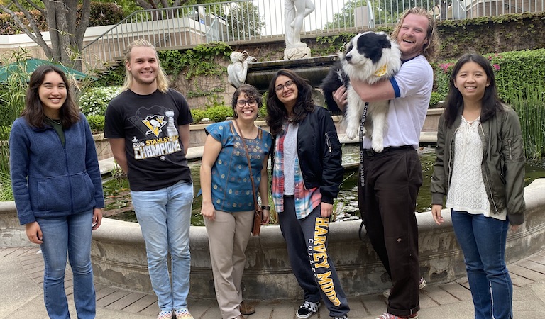 Prof. Hernandez-Castillo 2023 Spring research students standing in front of the pond including student holding black and white service dog