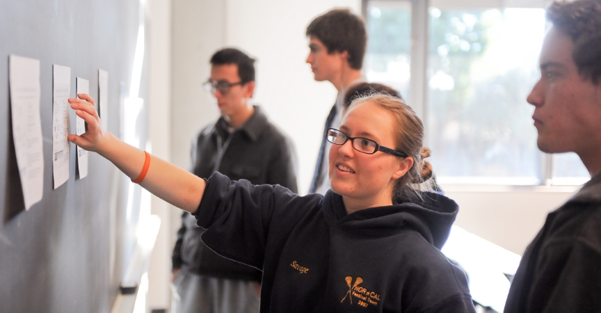 Students look at paper attached to chalk board