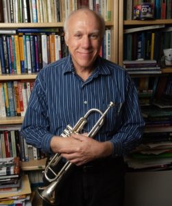 Bob Keller holding trumpet in front of book case.