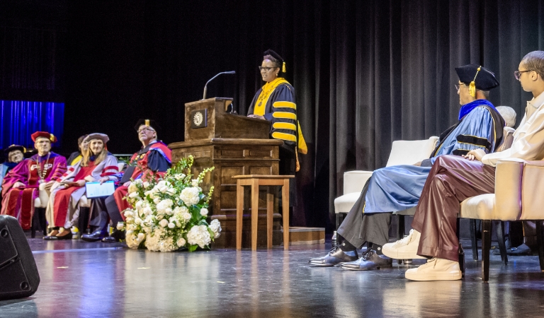 Harriet Nembhard at podium on stage with others seated either side of her.