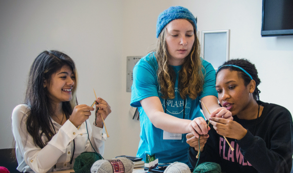 A student stands between two and assists with knitting.
