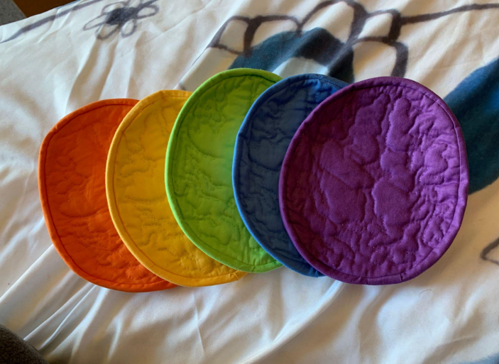 Five differently-colored potholders that are quilted to depict a brain.