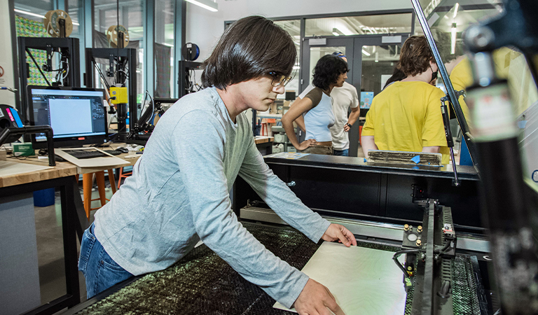 A Makerspace Steward prepares a large piece of paper on a machine.