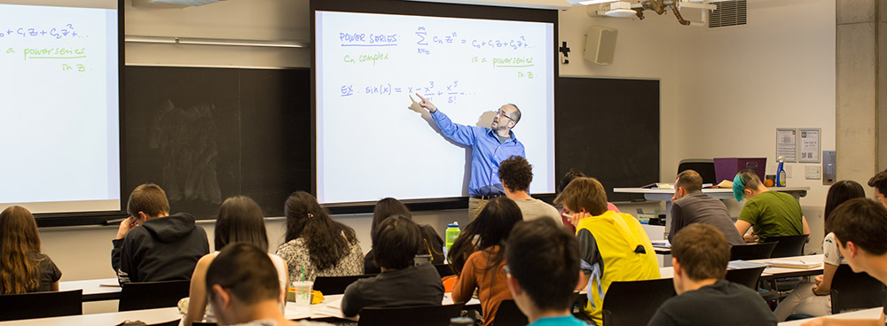 a professor teaching math functions in front of a college classroom