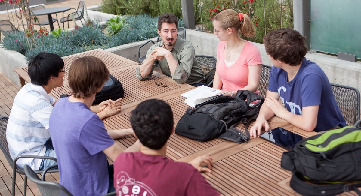 Prof Orrison with 5 students talk at a table.