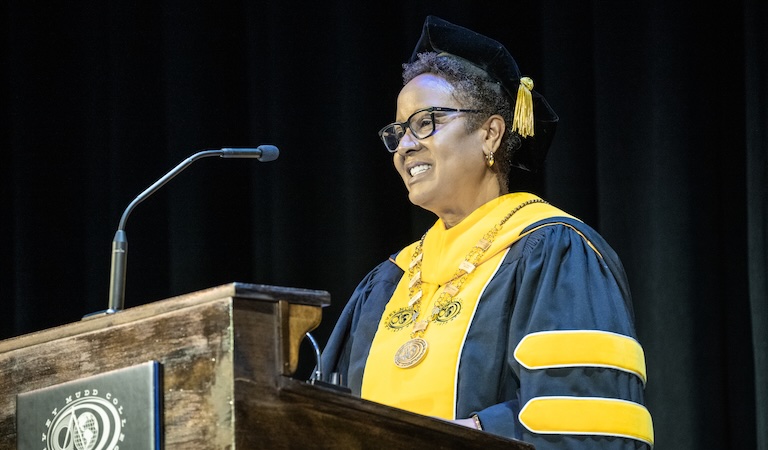 Harriet Nembhard in academic robes at a lecturn.