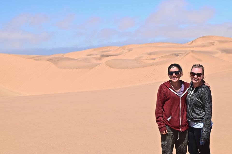Two students in front of sand dunes.